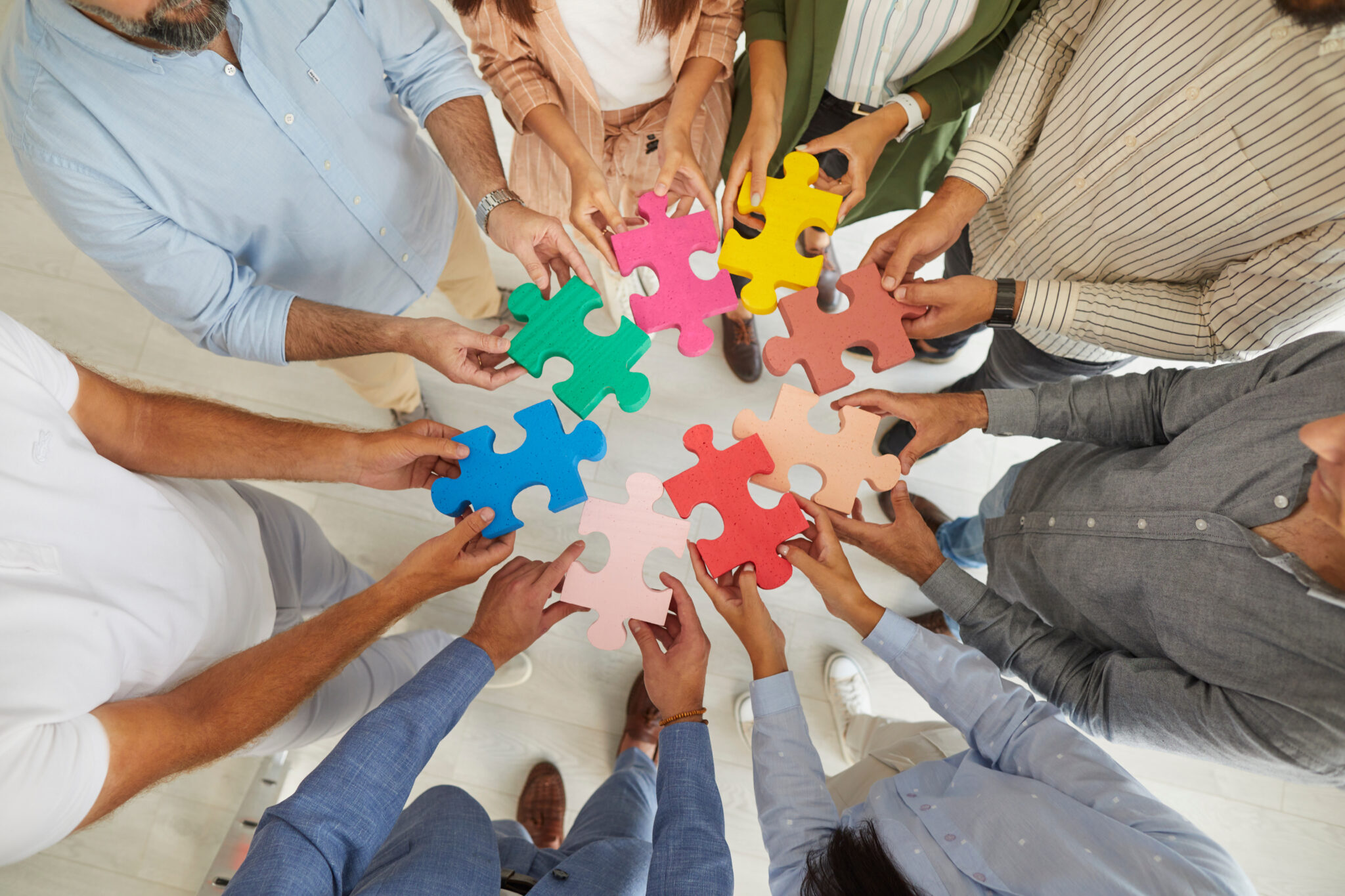 Team of creative senior and young business people joining pieces of colorful jigsaw puzzle as symbol and metaphor for teamwork and looking for professional solutions together, top view, close up